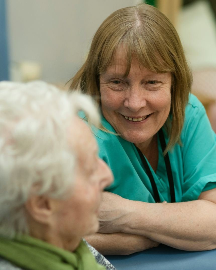 A nurse smiling as she leans in to talk with an older woman at home