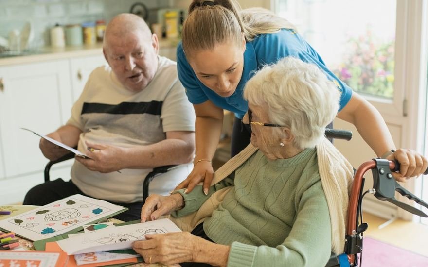 A caregiver helping two older people with an activity at the kitchen table